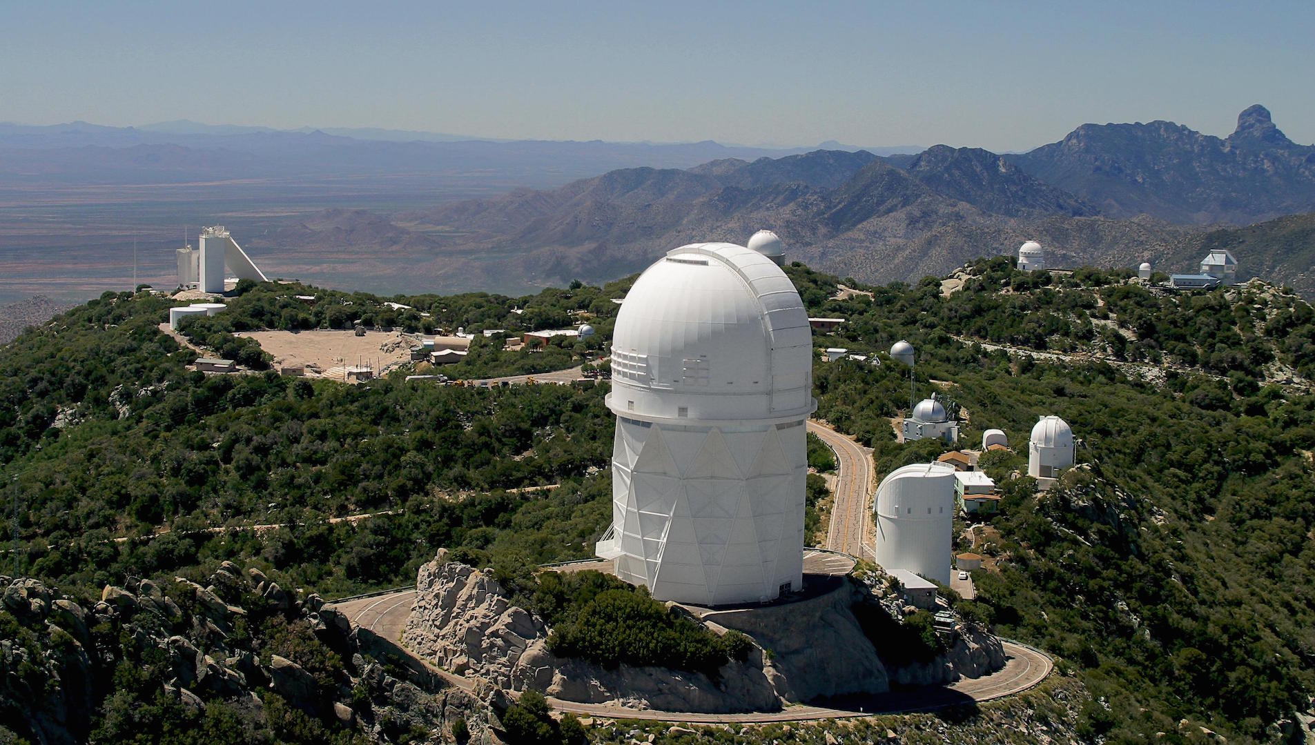 White domes and optical telescopes on the mountain peaks above the desert below.