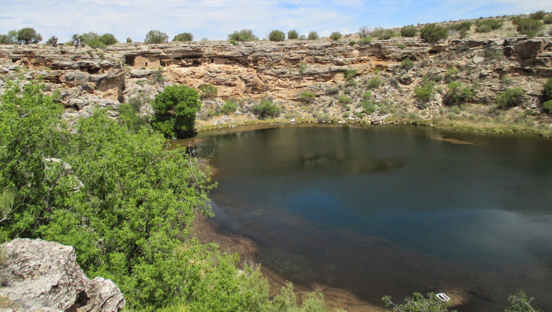 Ancient cliff dwelling is perched above the waters of an oasis desert sinkhole.
