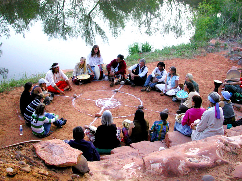 A group seated on a creek-side beach, gathered for a Native American medicine wheel ceremony.