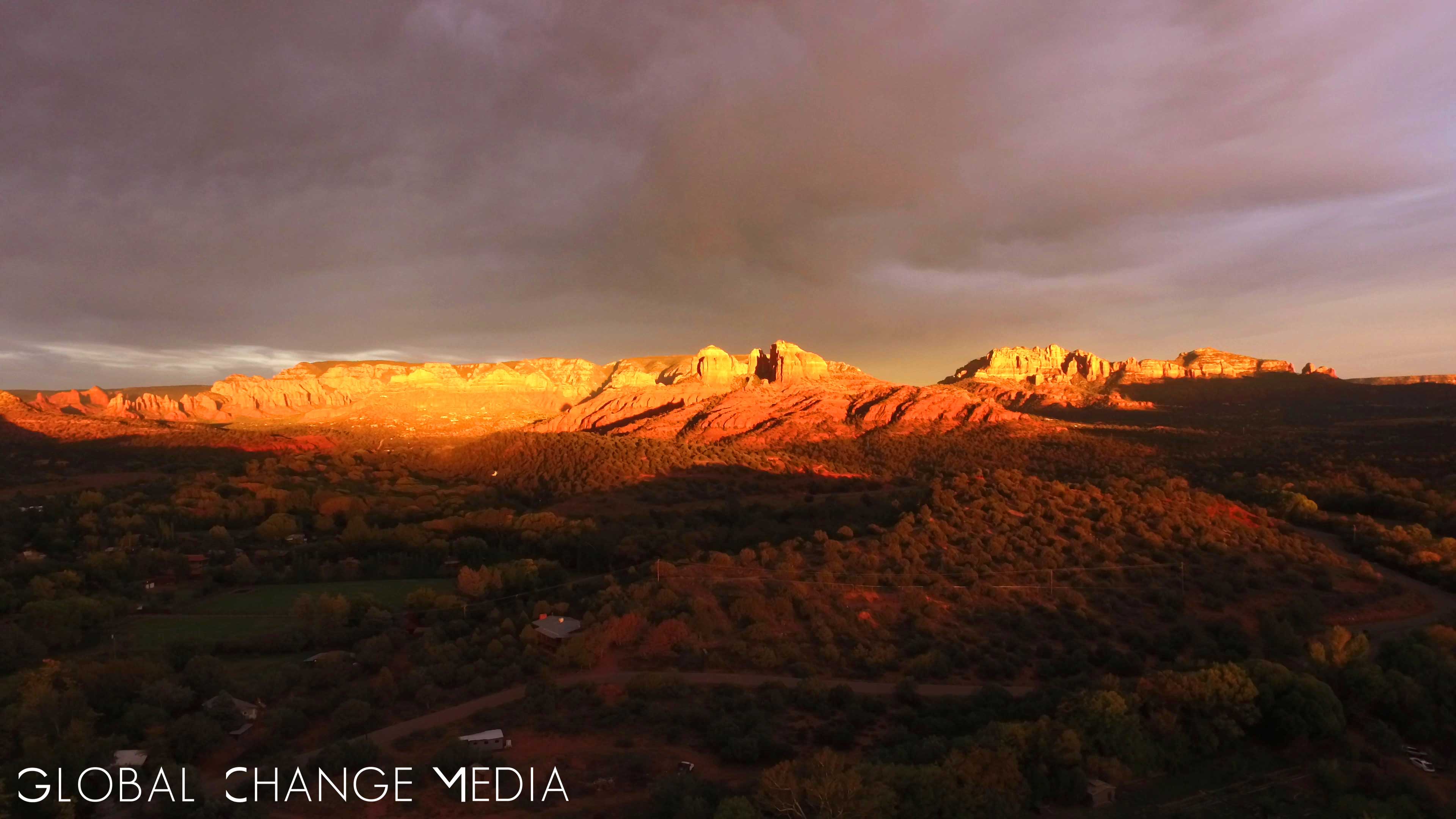 Under ominous clouds in a darkened sky, the red rock spires of Sedona are ignited by the afterglow of twilight.